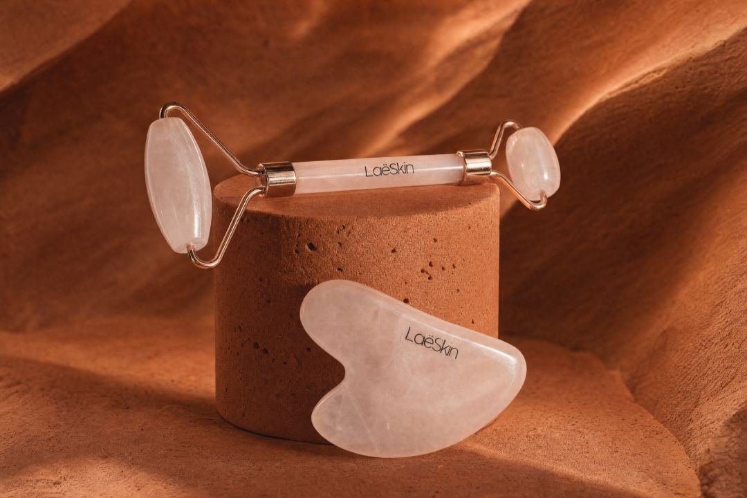 Rouleau et gua sha en quartz rose sur un socle terre cuite, fond orangé