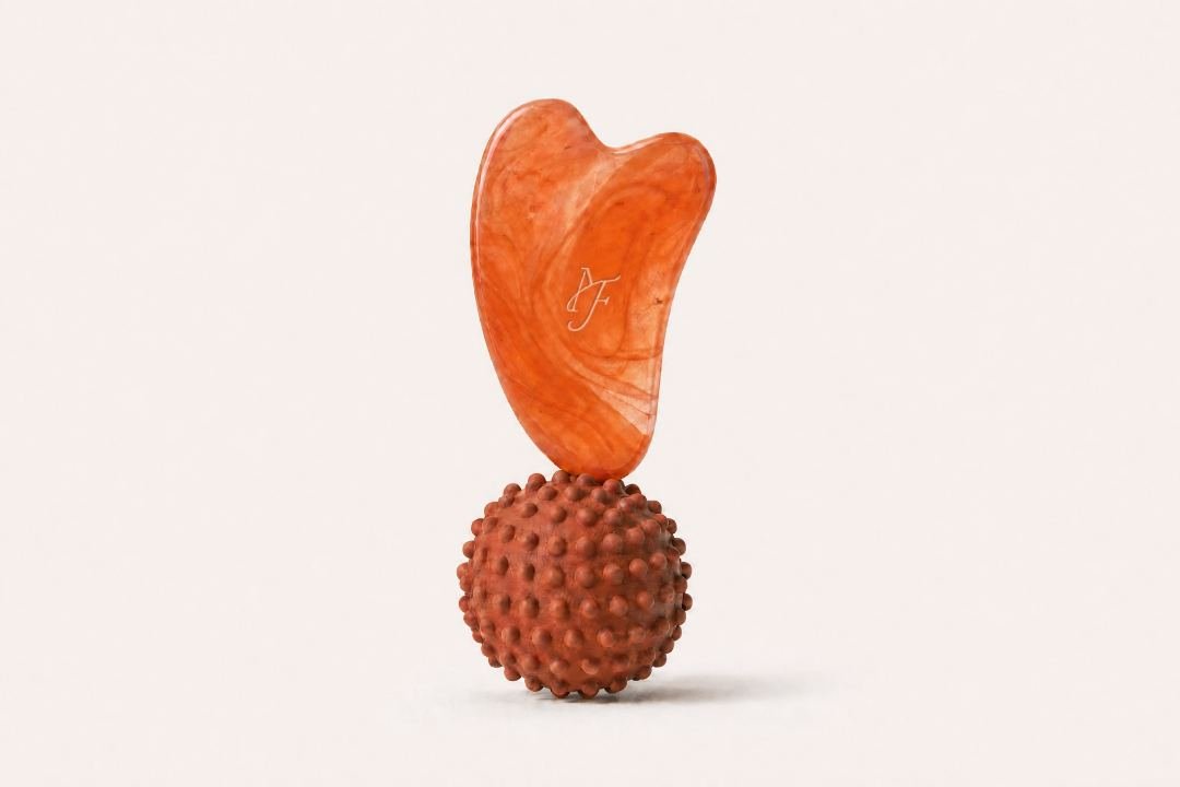 Gua sha orange et boule de massage sur fond blanc